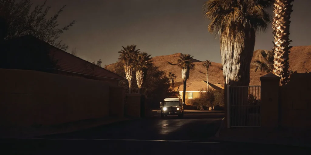 Security patrol vehicle driving through a gated community entrance in Riverside County with suburban homes and palm trees